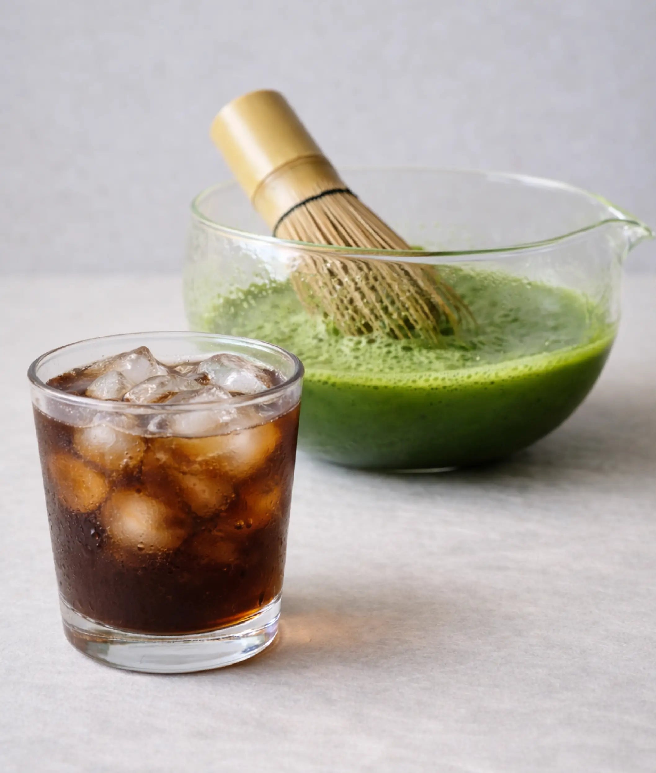 Photo of iced coffee and matcha with whisk in glass chawan full of matcha