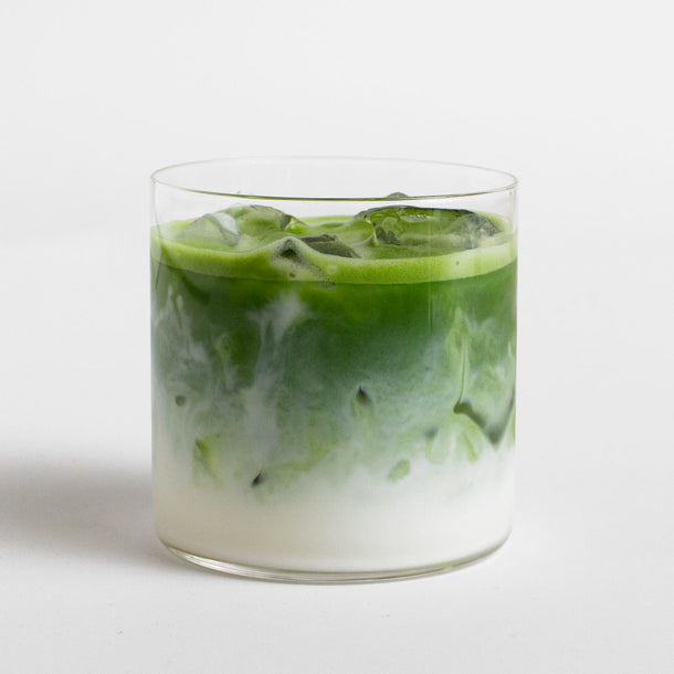 Glass of ceremonial organic iced green tea with milk on a white background