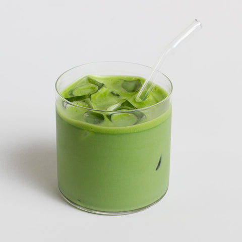 Organic ceremonial grade matcha Green tea iced drink in a glass with a straw on a white background