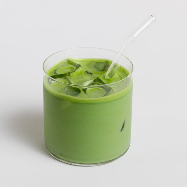 Organic ceremonial grade matcha Green tea iced drink in a glass with a straw on a white background