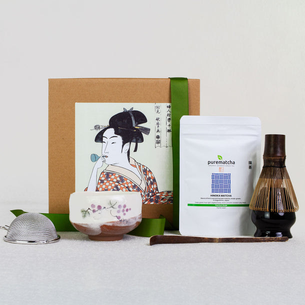 Tea set with a box featuring an illustration of a geisha, a white container labeled 'purematcha', and a wooden scoop on a light gray background.