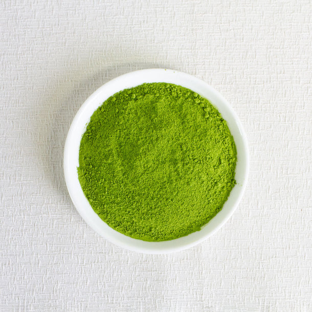 Organic matcha Green powder in a white bowl on a light fabric background