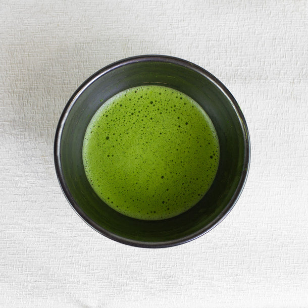 Green matcha tea in a black bowl on a white fabric background