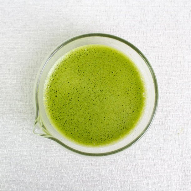 Green matcha tea in a glass chawan with spout on a white background