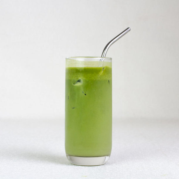 Glass of matcha iced latte drink with a metal straw on a white background