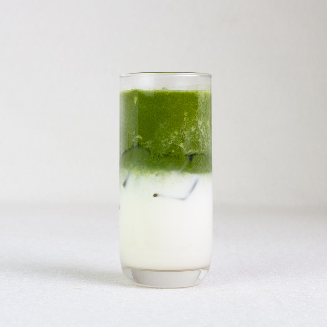 Glass with a layered drink of green and white on a white background