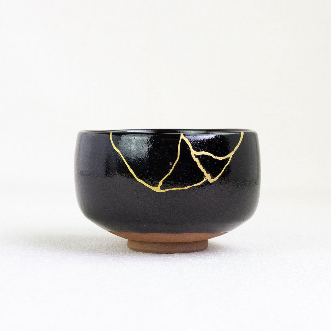 Black ceramic bowl with gold repair on a white background