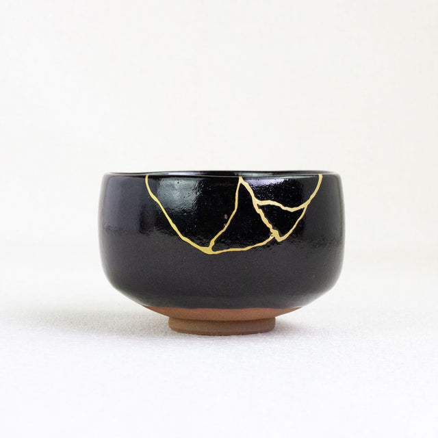 Black ceramic bowl with gold repair on a white background