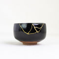 Black ceramic bowl with gold repair on a white background
