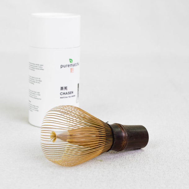 Bamboo whisk and container labeled 'purematcha' on a white background