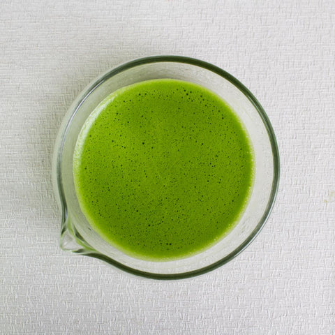 ceremonial grade matcha tea whisked in a glass tea bowl with spout on a white background
