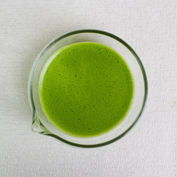 ceremonial grade matcha tea whisked in a glass tea bowl with spout on a white background