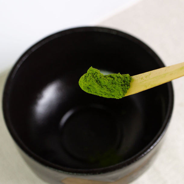 Matcha green tea powder on a wooden spoon over a black bowl