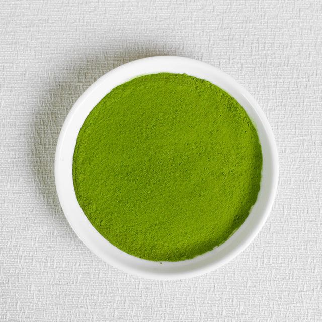 Ceremonial Grade Organic Matcha Green powder in a white bowl on a textured white background