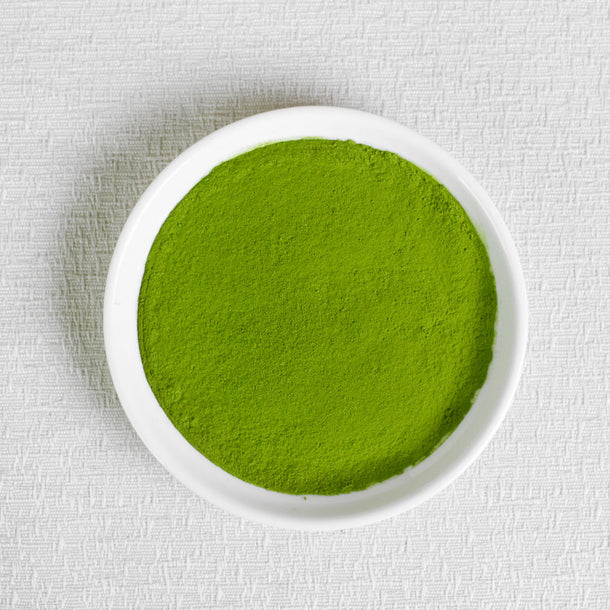 Pure matcha ceremonial grade organic Japanese Green powder in a white bowl on a textured white background