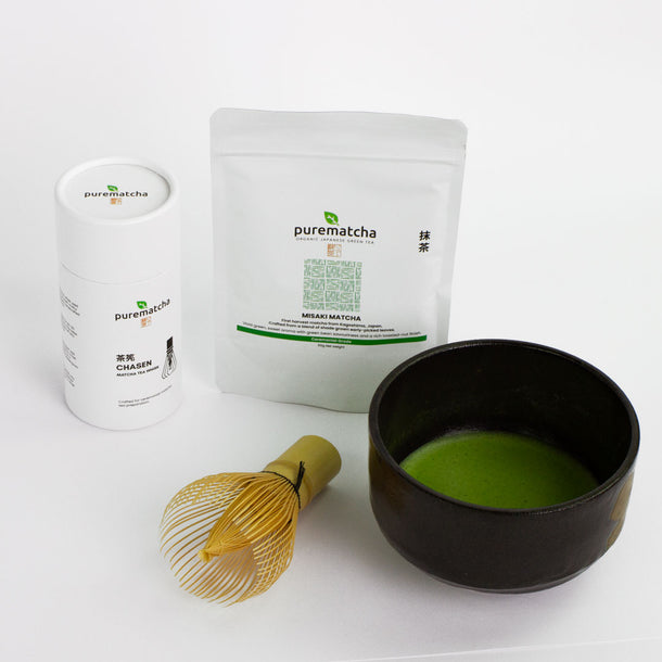 Matcha green tea set with containers, a bowl of matcha, and a whisk on a white background