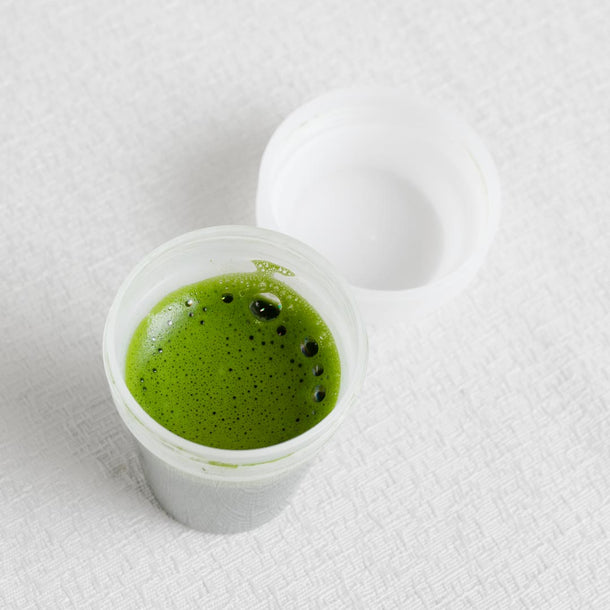 Small plastic cup with green liquid on a white textured surface