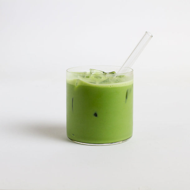 Green iced drink in a glass with a straw on a white background